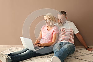 Mature couple with laptop sitting on floor in empty room. Moving into new house