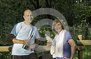 Mature couple leaninglooking to camera after doing exercise in the park holding reusable metal bottles