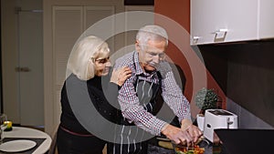 Mature couple in love making dinner. Elderly woman hugging from back husband cooking meal in kitchen