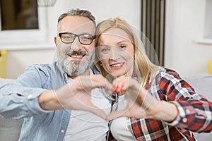 Mature couple making heart shape with hands on couch