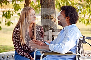 Mature Couple With Man Sitting In Wheelchair Talking  In Park Together