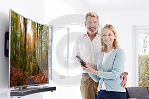 Mature Couple With New Curved Screen Television At Home