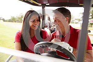 Mature Couple Playing Golf Marking Scorecard In Buggy Driving Along Course