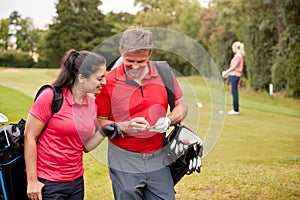 Mature Couple Playing Round Of Golf Carrying Golf Bags And Marking Scorecard