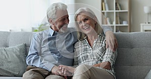 Mature couple posing for camera seated on couch at home