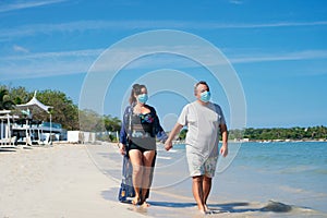 Couple with protective mask holding hands and strolling on the beach