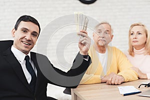 Mature couple at a reception with a lawyer. The lawyer holds a bundle of money and smiles.