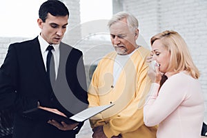 Mature couple at a reception with a lawyer. The lawyer reads a document. The old people are upset.