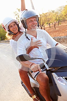 Mature Couple Riding Motor Scooter Along Country Road