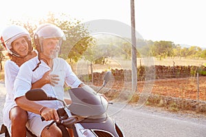 Mature Couple Riding Motor Scooter Along Country Road