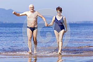 Mature couple runs on the water along the wild beach on a hot summer day