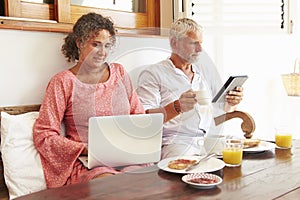 Mature Couple Sitting At Breakfast Table With Digital Devices