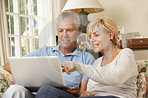 Mature Couple Sitting On Sofa At Home Using Laptop