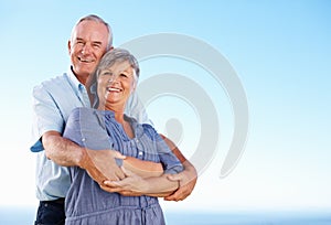 Mature couple smiling outdoors. Portrait of happy mature couple smiling together against blue sky.