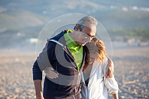 Mature couple in sportswear hugging while walking along shore