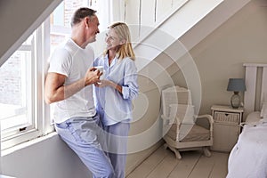 Mature Couple Standing By Bedroom Window With Hot Drink