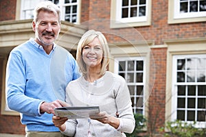 Mature Couple Standing Outside House Looking At Property Details