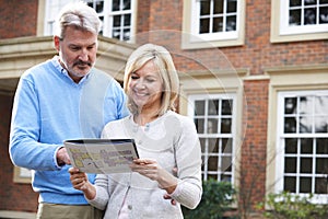 Mature Couple Standing Outside House Looking At Property Details