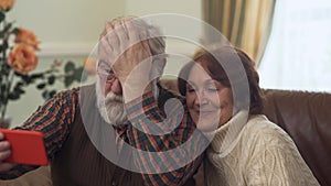 Mature couple taking selfie on cell phone. Old man corrects his hair, his wife sits closer. Leisure of progressive