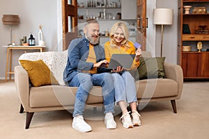 Mature Couple Using Laptop Computer And Bank Card At Home