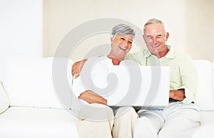 Mature couple using laptop on couch. Happy mature couple using laptop while sitting on couch.