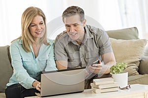 Mature Couple Using Mobile Phone And Laptop On Sofa