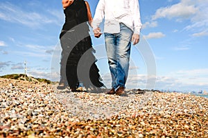 Mature couple walking on the beach by the hand of day