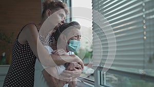 Mature daughter visiting senior mom in nursing home. Elderly daughter hugs her 90 year old mother in medical mask while