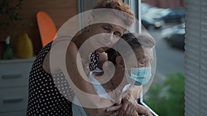 Mature daughter visiting senior mom in nursing home. Elderly daughter hugs her 90 year old mother in medical mask while