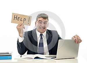 Mature desperate businessman suffering stress working at computer desk holding sign asking for help looking stressed overworked