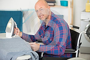 Mature disabled man on wheelchair ironing clothing