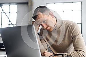 Mature disappointed businessman sitting at the laptop and watching at the computer screen