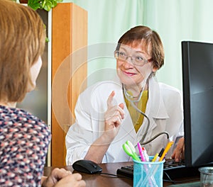 Mature doctor behind computer with patient