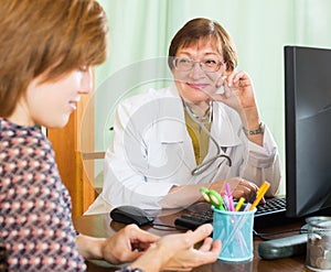 Mature doctor behind computer with patient