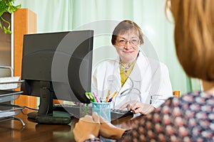 Mature doctor behind computer with patient