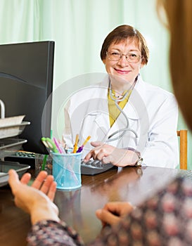 Mature doctor behind computer with patient