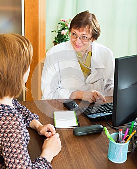 Mature doctor behind computer with patient