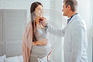 Mature doctor checking lymph nodes of pregnant woman