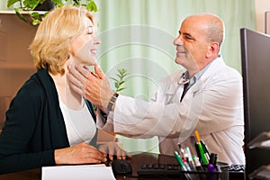 Mature doctor checking thyroid of smiling woman