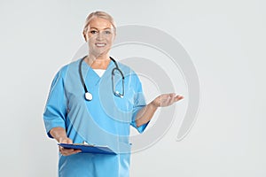 Mature doctor with clipboard on grey background. Space for text