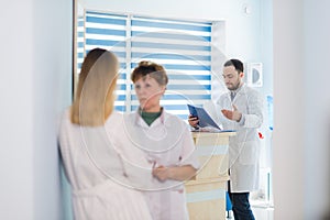 Mature doctor discussing with nurses in a hallway hospital. Doctor discussing patient case status with his medical staff