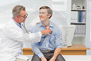 Mature doctor listening to his happy patients chest with stethoscope