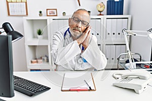 Mature doctor man at the clinic sleeping tired dreaming and posing with hands together while smiling with closed eyes