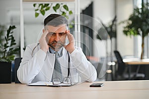 Mature doctor man at the clinic tired rubbing nose and eyes feeling fatigue and headache. stress and frustration concept