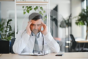 Mature doctor man at the clinic tired rubbing nose and eyes feeling fatigue and headache. stress and frustration concept