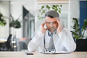 Mature doctor man at the clinic tired rubbing nose and eyes feeling fatigue and headache. stress and frustration concept