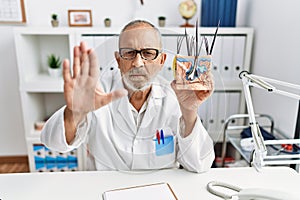 Mature doctor man holding model of human anatomical skin and hair with open hand doing stop sign with serious and confident