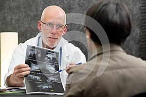 Mature doctor and woman patient looking at Xray in medical office