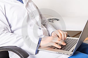 Mature doctor working on laptop and medication`s cases to make prescriptions in his clinic office. Man preparing online internet