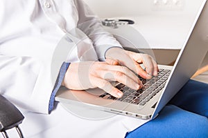 Mature doctor working on laptop and medication`s cases to make prescriptions in his clinic office. Man preparing online internet